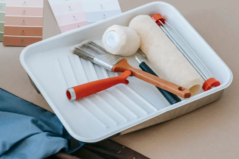 A paint tray with a roller and two brushes.