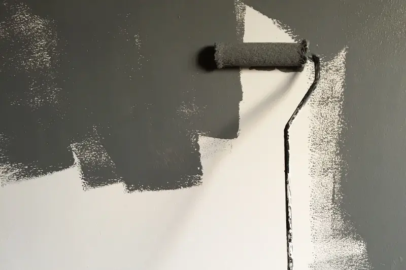 A roller with grey paint on a partially painted wall.